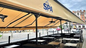 An outdoor seating area with a canopy labeled "SPA" and a view of the street. - Hôtel-Restaurant L’Auberge (Spa)
