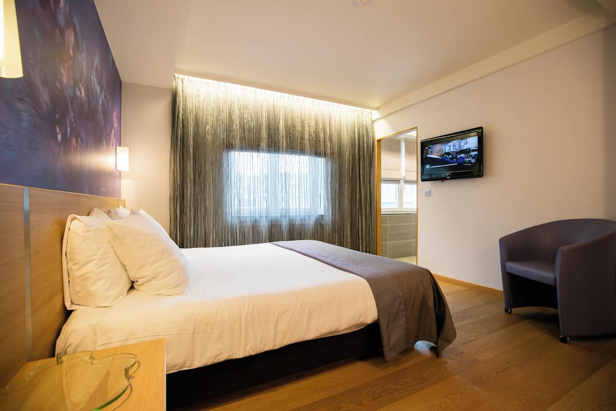 A hotel room with a bed, a TV on the wall, a chair, and a window with curtains.