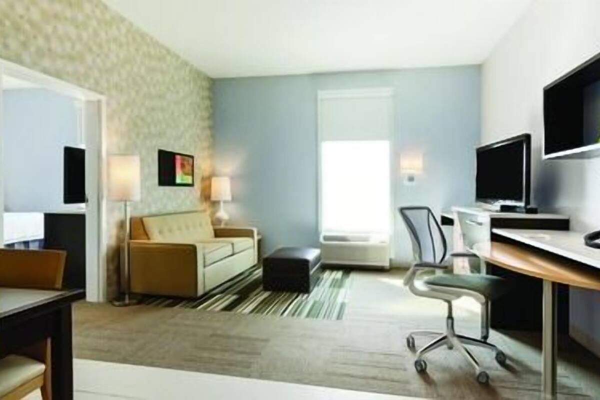 A hotel room with a sofa, a desk, a chair, a TV, and a window.