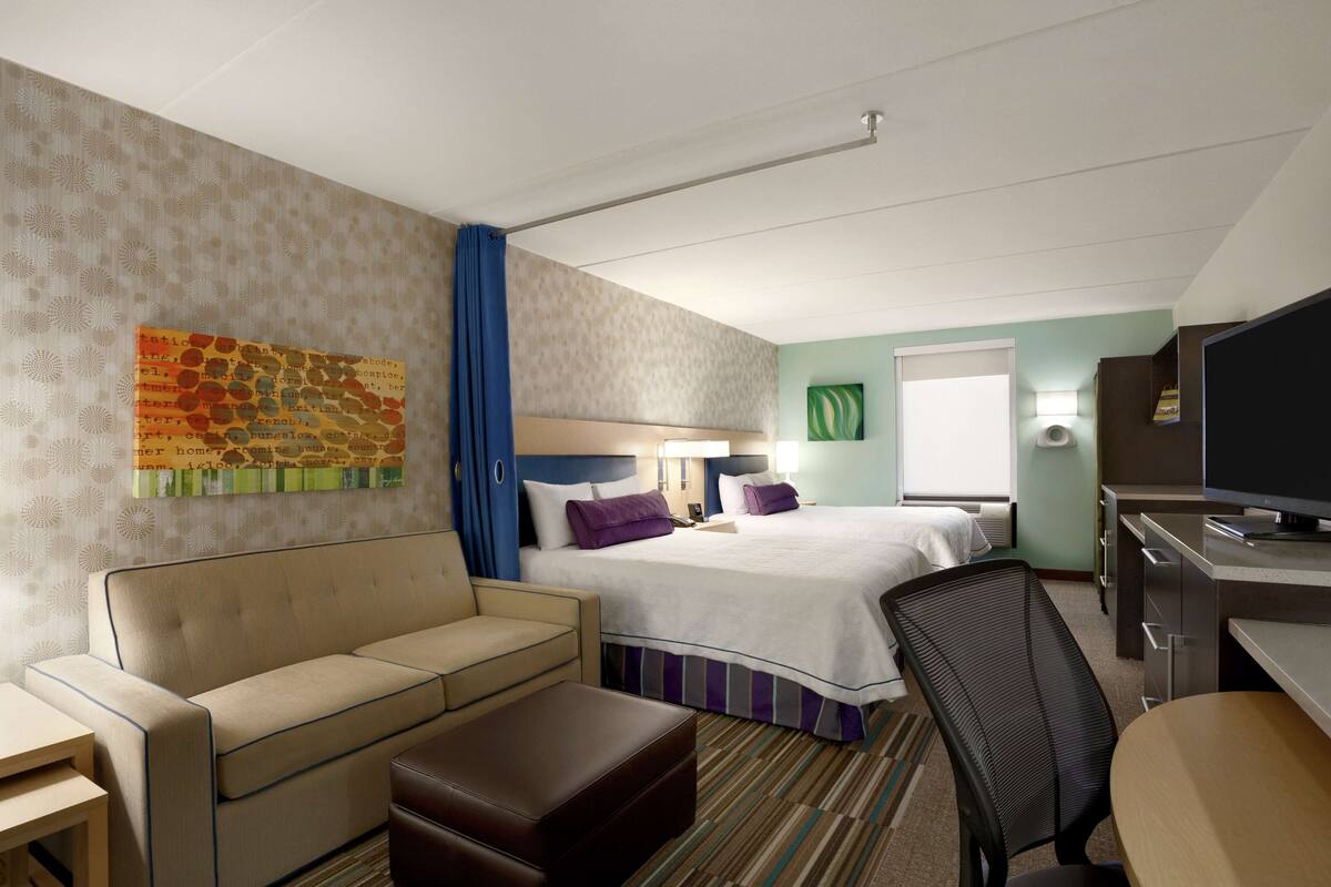 A hotel room with a bed, a sofa, a desk, and a television.