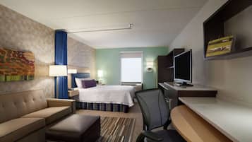 A hotel room with a bed, a sofa, a desk, a TV, and a window.