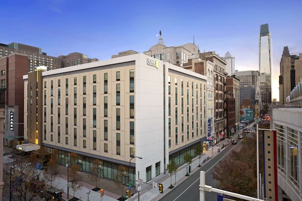 Un hotel moderno con un llamativo rótulo que dice 'HOTEL', rodeado de edificios urbanos y un cielo despejado.