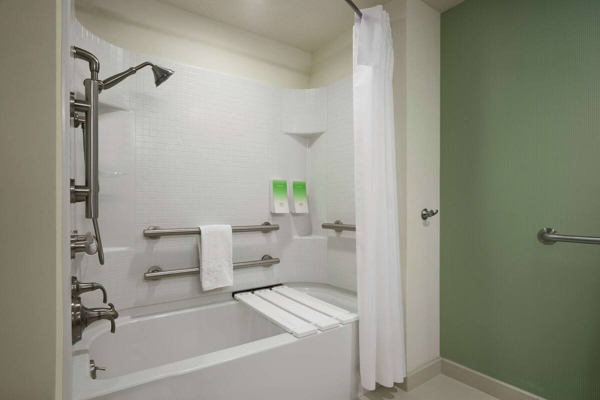 A bathroom with a bathtub, shower, and grab bars.