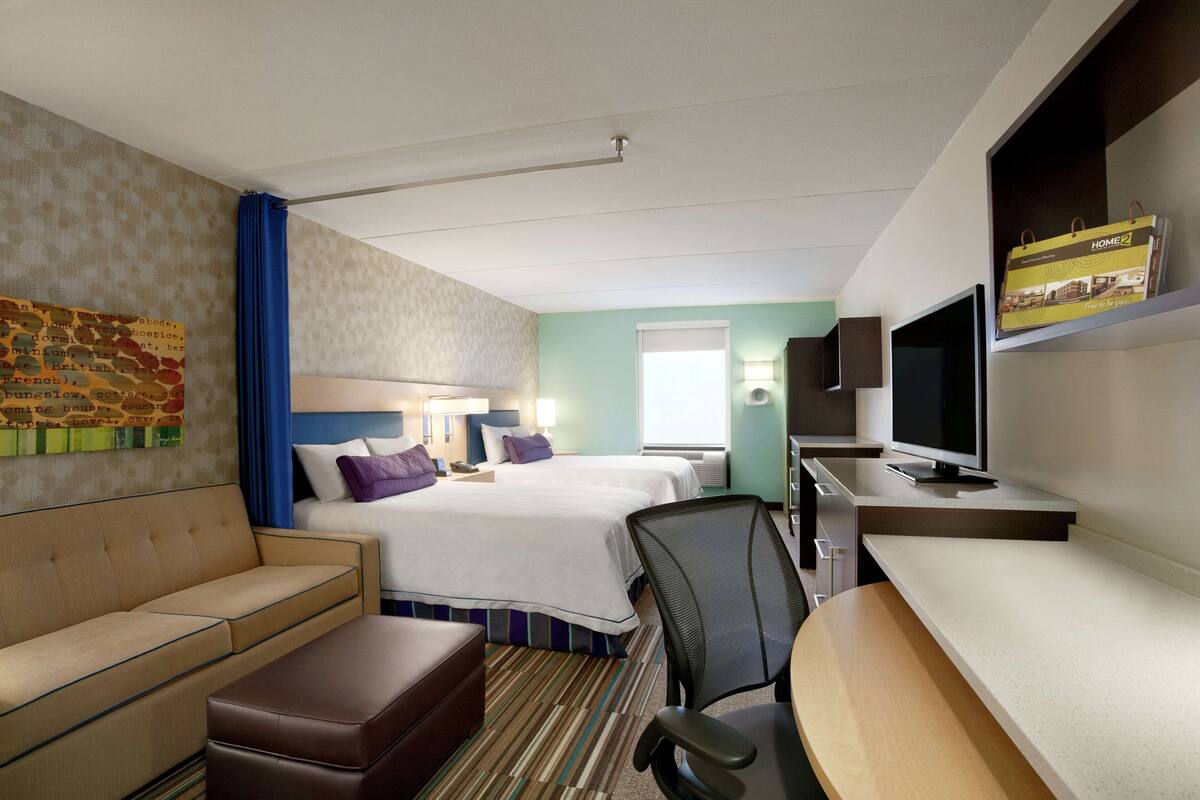 A hotel room with two beds, a sofa, a desk, and a TV.