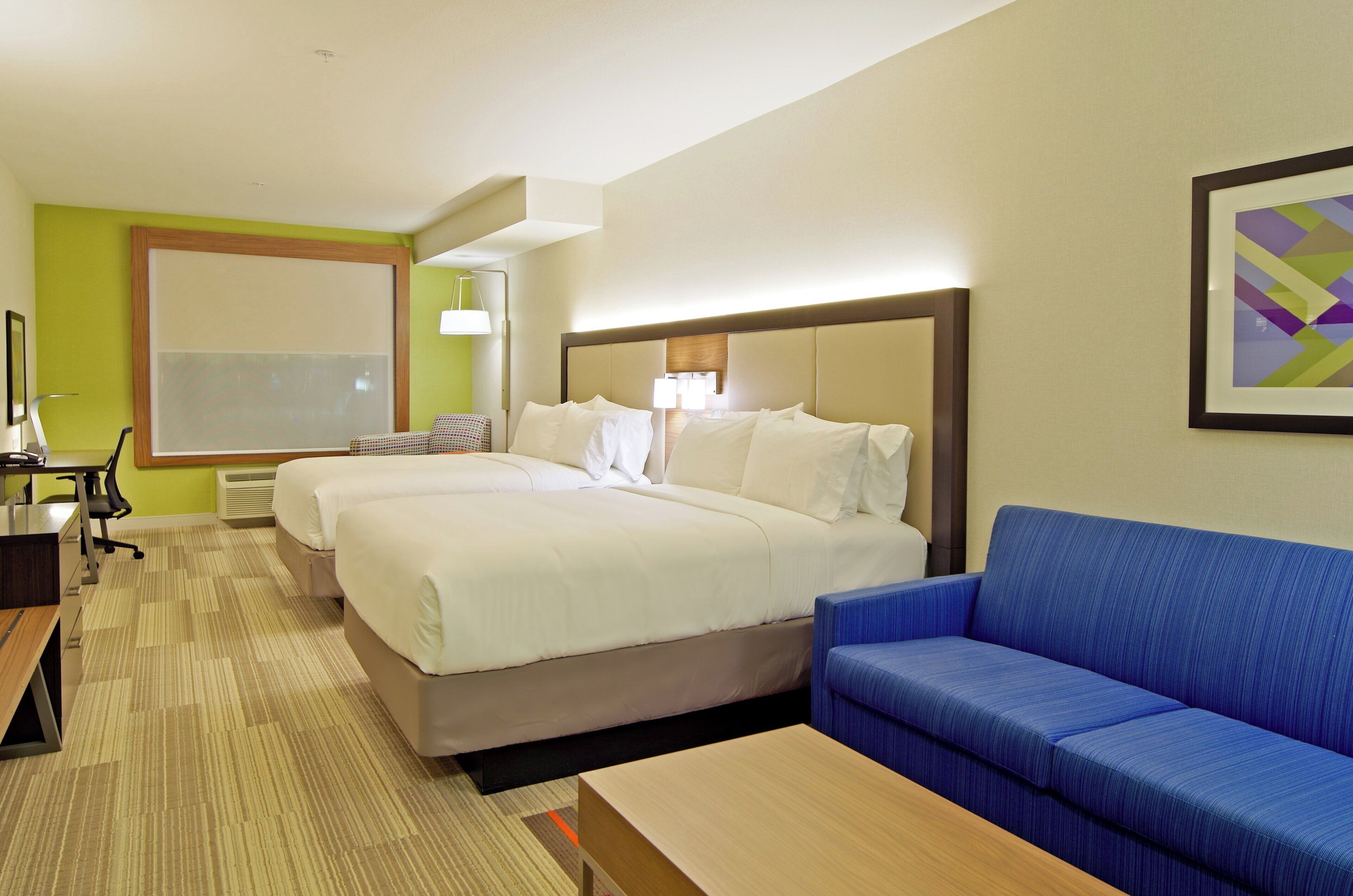 Habitació d'hotel amb dos llits, un escriptori, un sofà blau i una finestra gran.