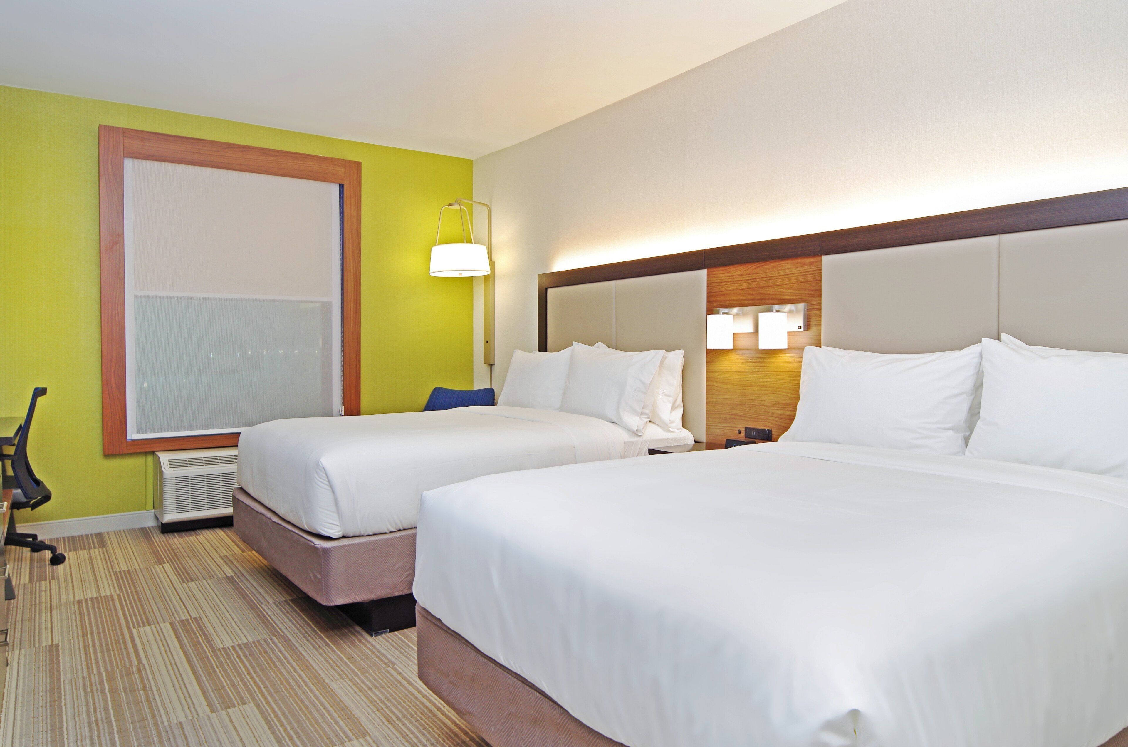 Habitación de hotel con dos camas, un ventanal grande, un escritorio y una silla.