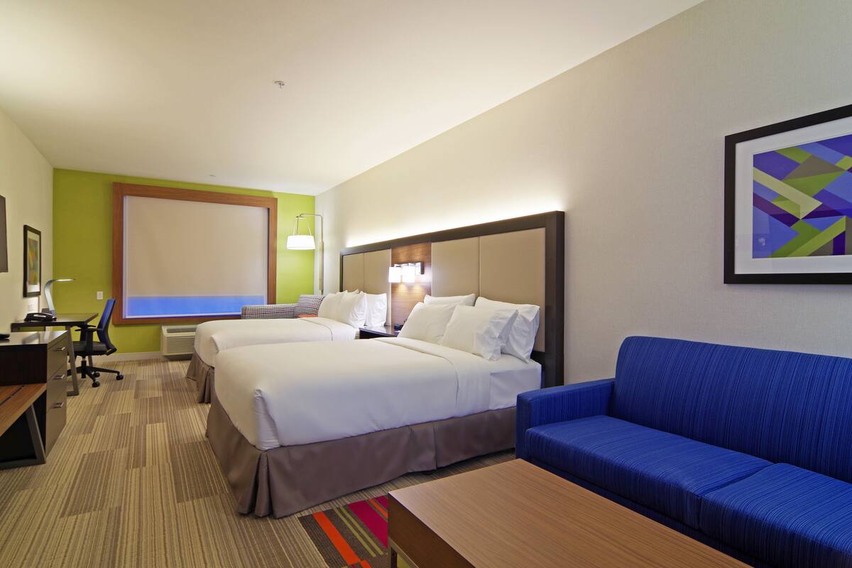 A hotel room with two beds, a desk, a chair, a sofa, and a large window.