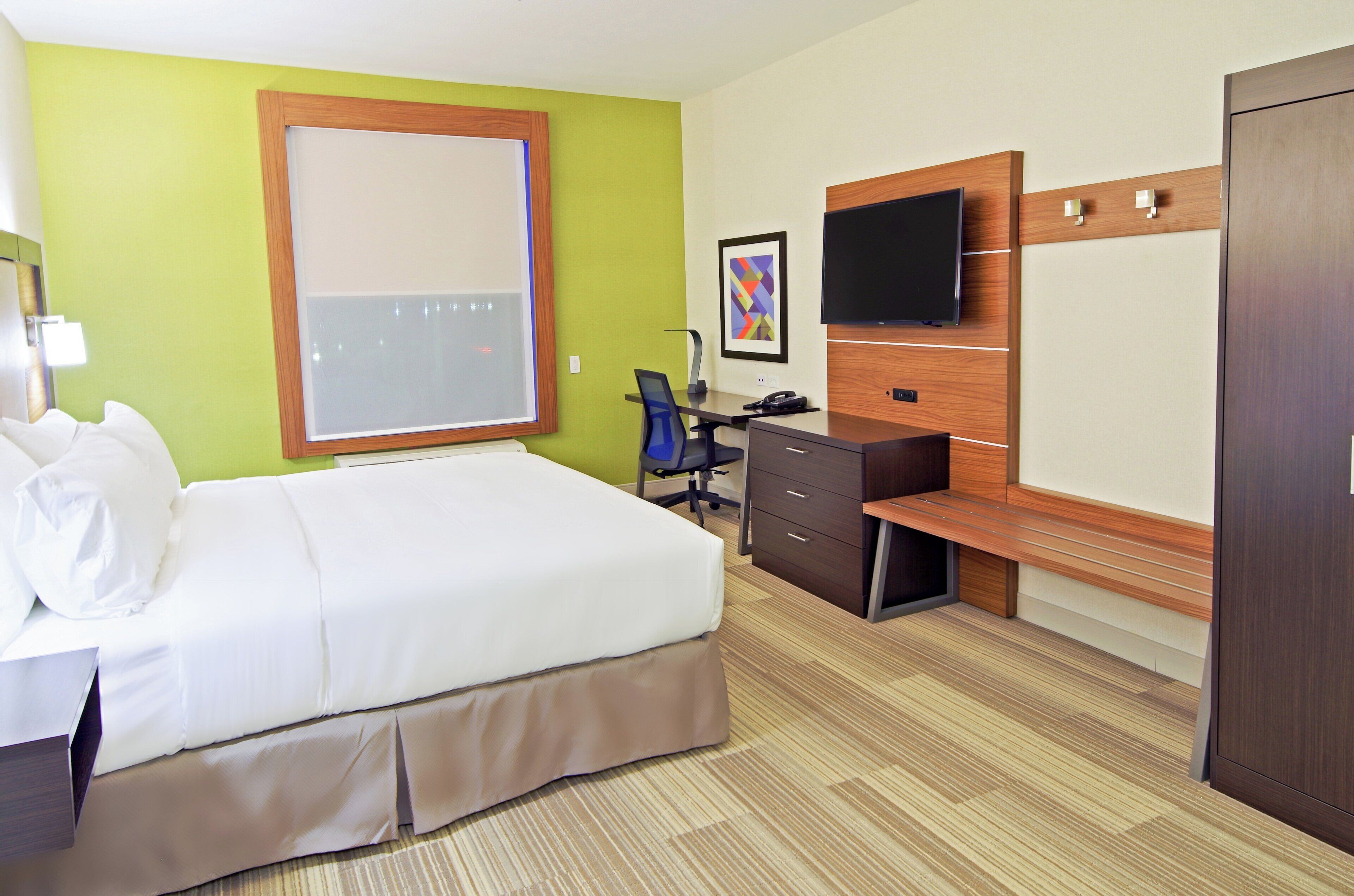 A hotel room with a bed, desk, chair, television, and wardrobe.