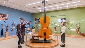Una exhibición en un museo con instrumentos musicales, incluyendo un gran violonchelo, rodeada de visitantes.