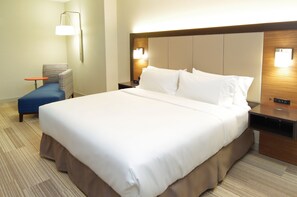 A hotel room with a large bed, a bedside table, a nightstand, a chair, and a wall-mounted lamp.