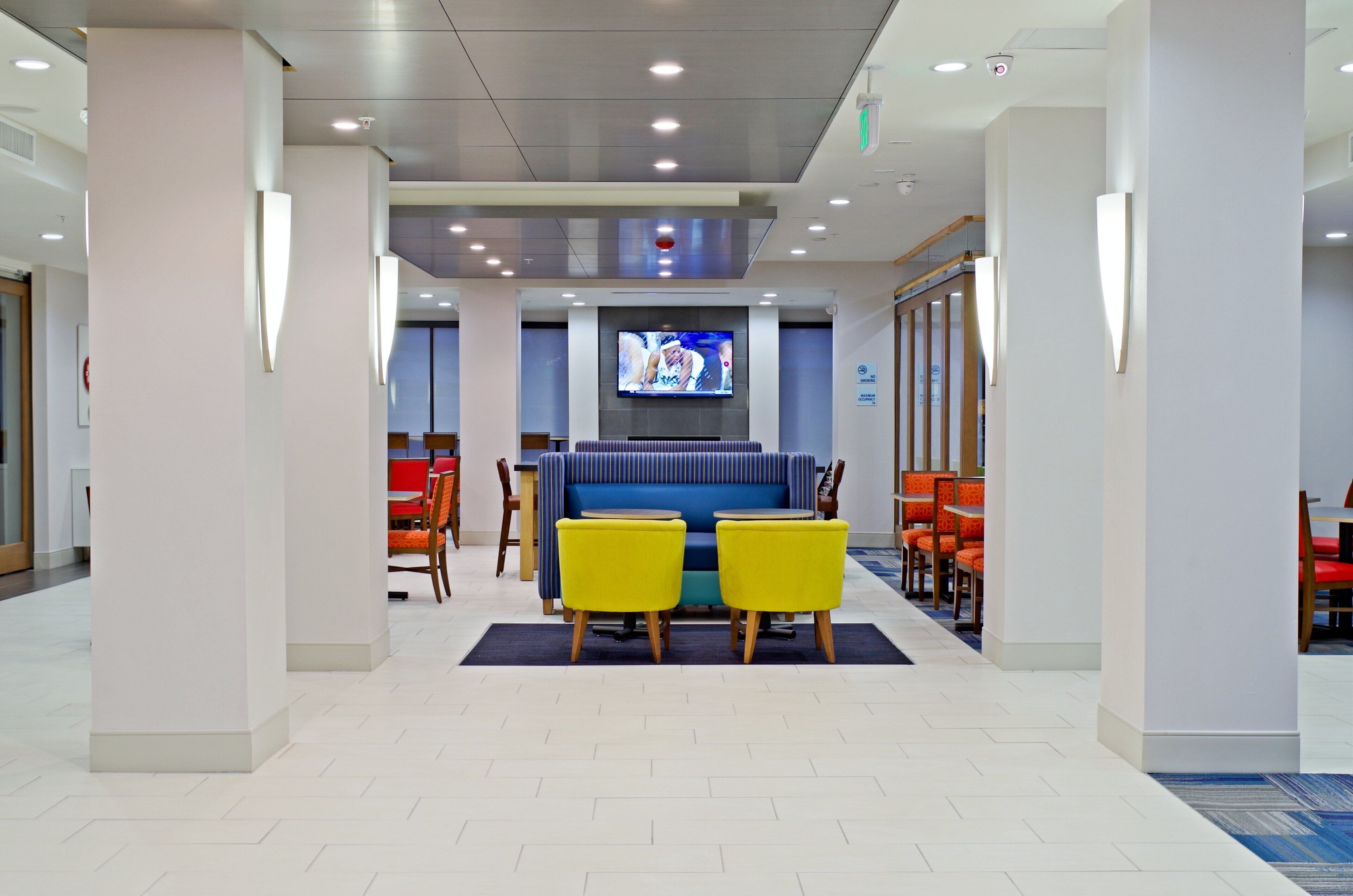 A lobby area with a seating area featuring yellow chairs, a blue sofa, and a television screen mounted on the wall.