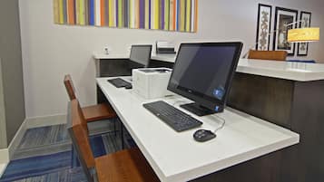 Een hotelwerkplek met meerdere computerwerkplekken, een printer en een bureaulamp.
