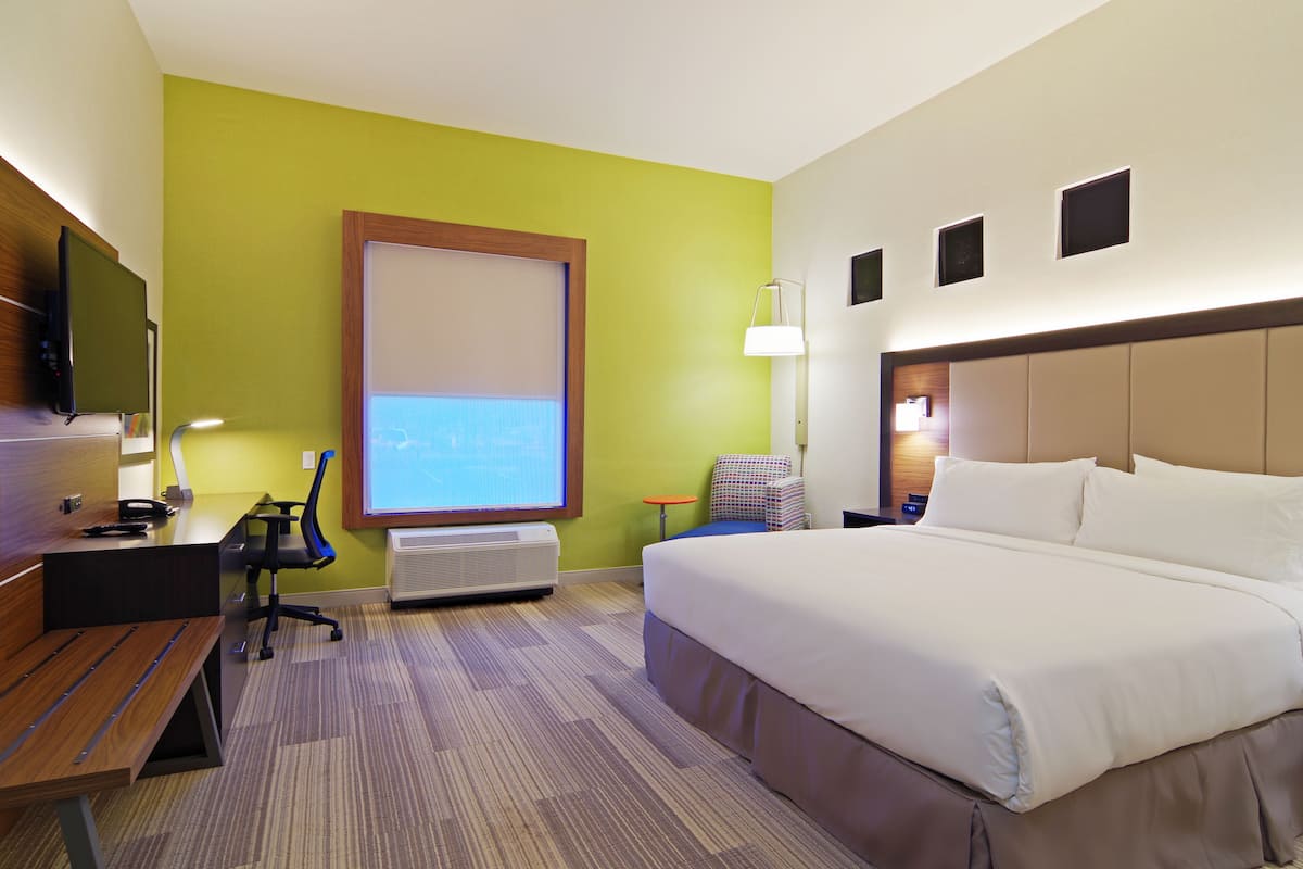 A hotel room with a large bed, a desk with a computer, a chair, a TV, and a projector screen.