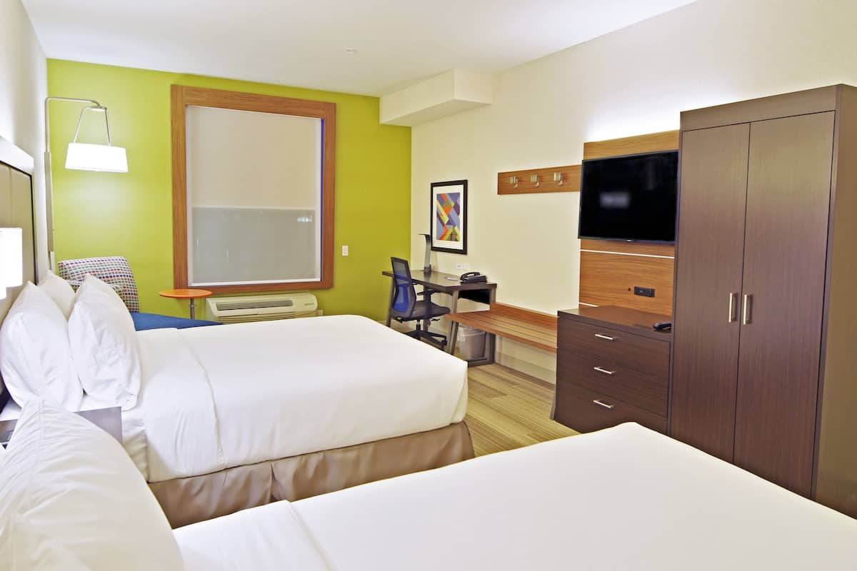 A hotel room with two beds, a desk, a chair, a TV, and a wardrobe.