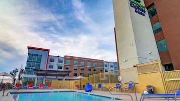 A hotel with a swimming pool, outdoor seating, and a clear sky.