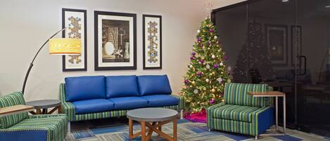 A modern living room with a blue sofa, green patterned armchairs, a round coffee table, and a Christmas tree.