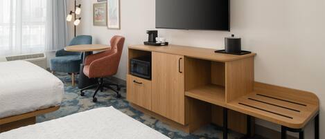 A hotel room with a bed, a desk with a computer, a chair, a TV, and a coffee maker.