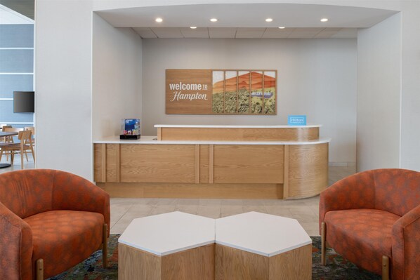 A reception area with a wooden reception desk, two orange armchairs, and a wall-mounted welcome sign. - Hampton Inn by Hilton North Hollywood (North Hollywood)