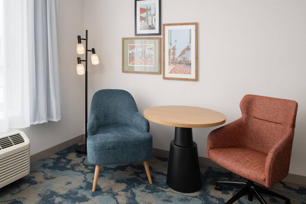 A room with a blue armchair, a wooden table, and a red armchair. There are three framed pictures on the wall.