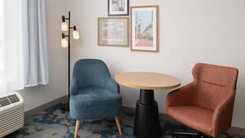 A room with a blue armchair, a wooden table, and a red armchair. There are three framed pictures on the wall.