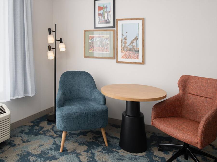A room with a blue armchair, a wooden table, and a red armchair. There are three framed pictures on the wall.