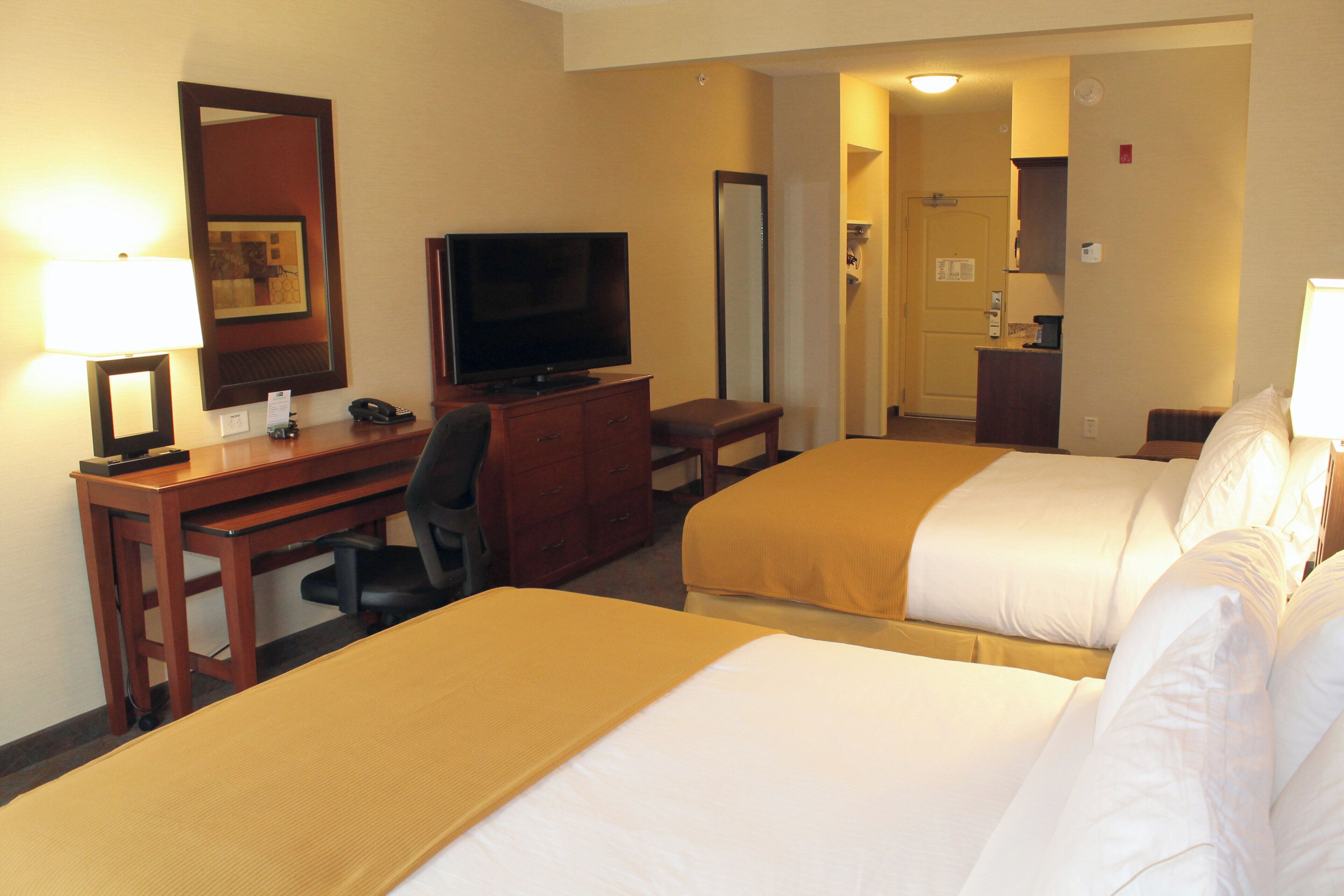 A hotel room with two beds, a desk, a television, and a mirror.