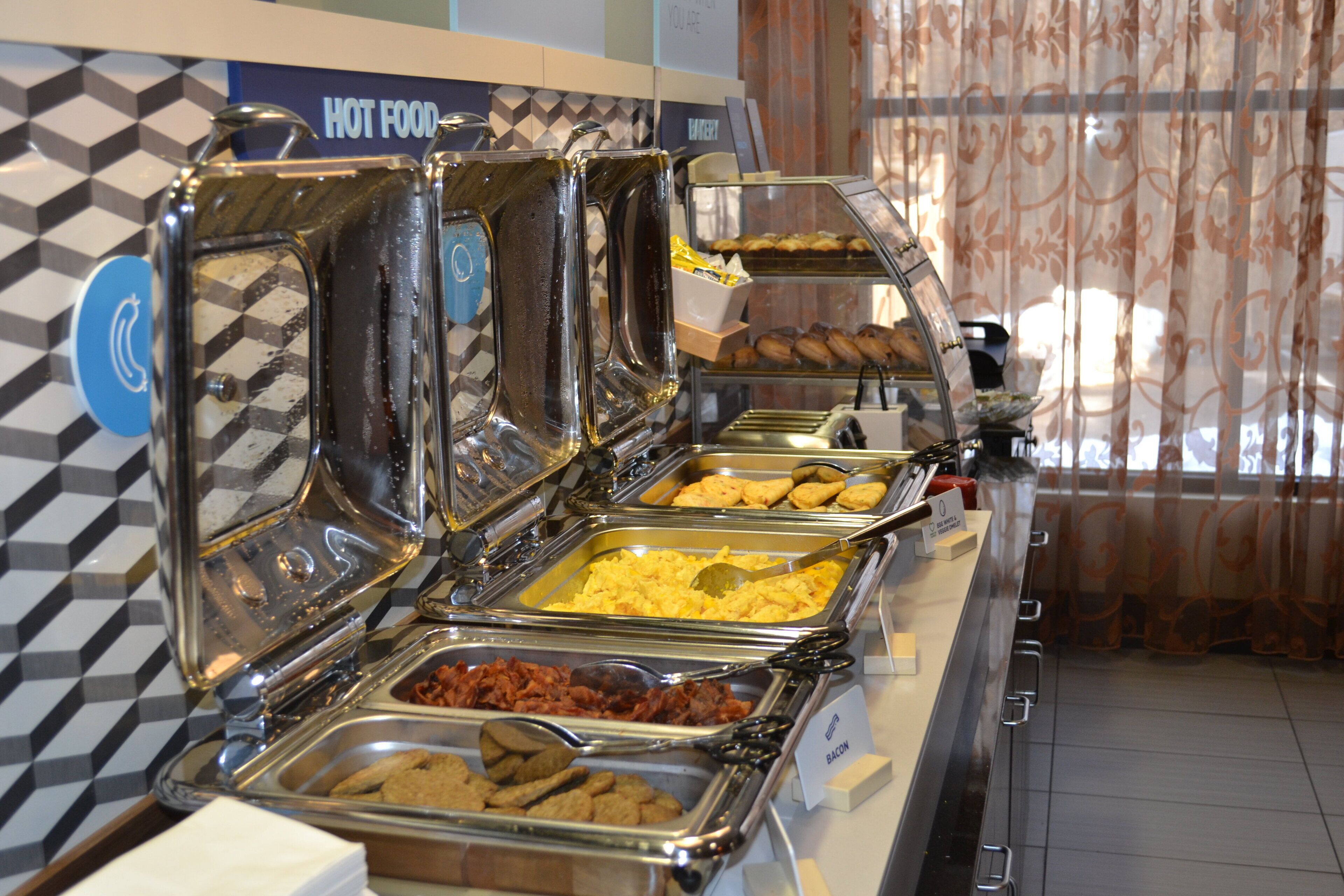 Buffet com diversas opções de comida, incluindo ovos mexidos, bacon e doces.
