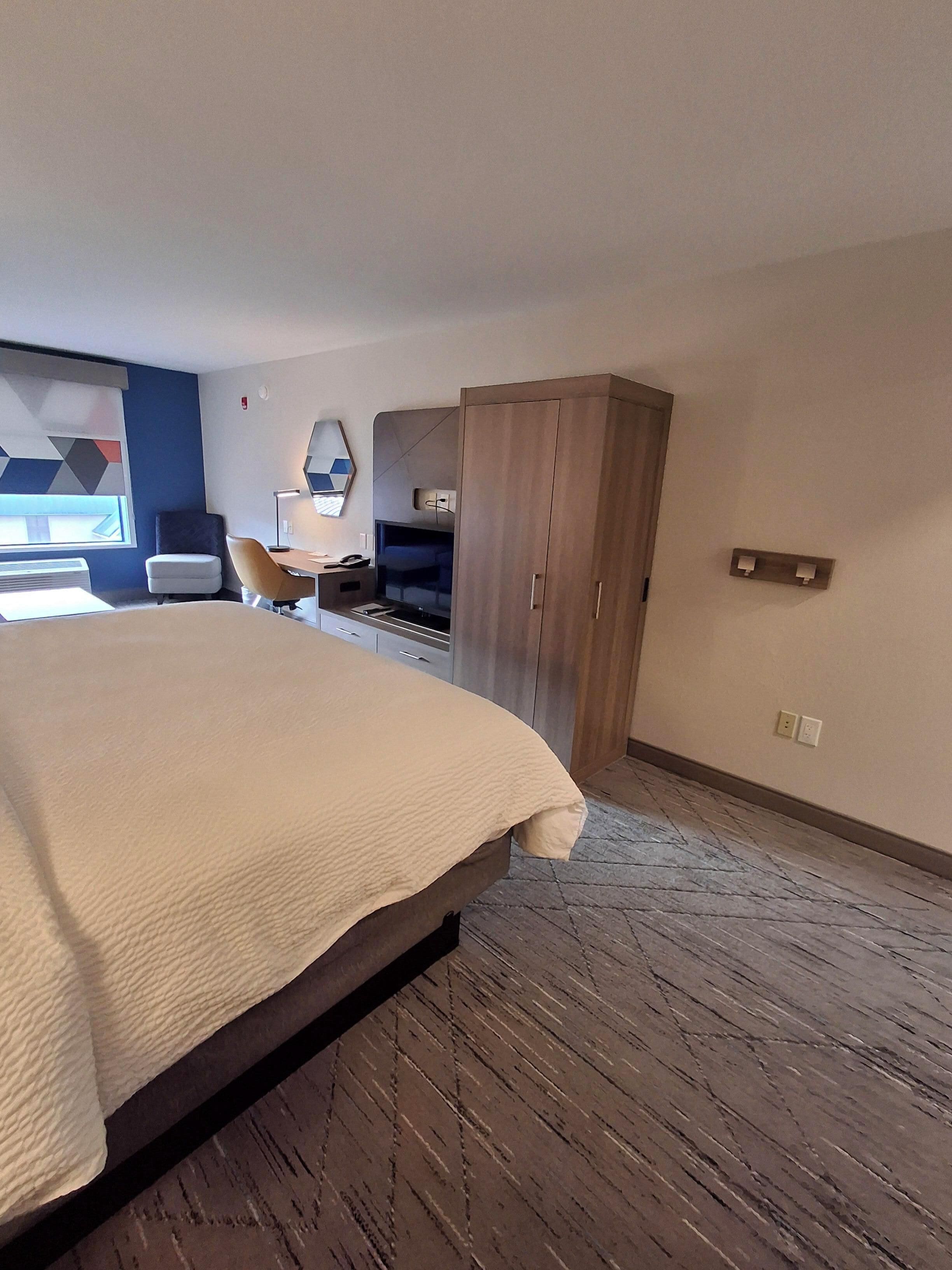 Une chambre d’hôtel avec un grand lit, un bureau avec une chaise, une armoire et un téléviseur fixé au mur.