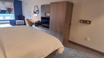 Une chambre d’hôtel avec un grand lit, un bureau avec une chaise, une armoire et un téléviseur fixé au mur.