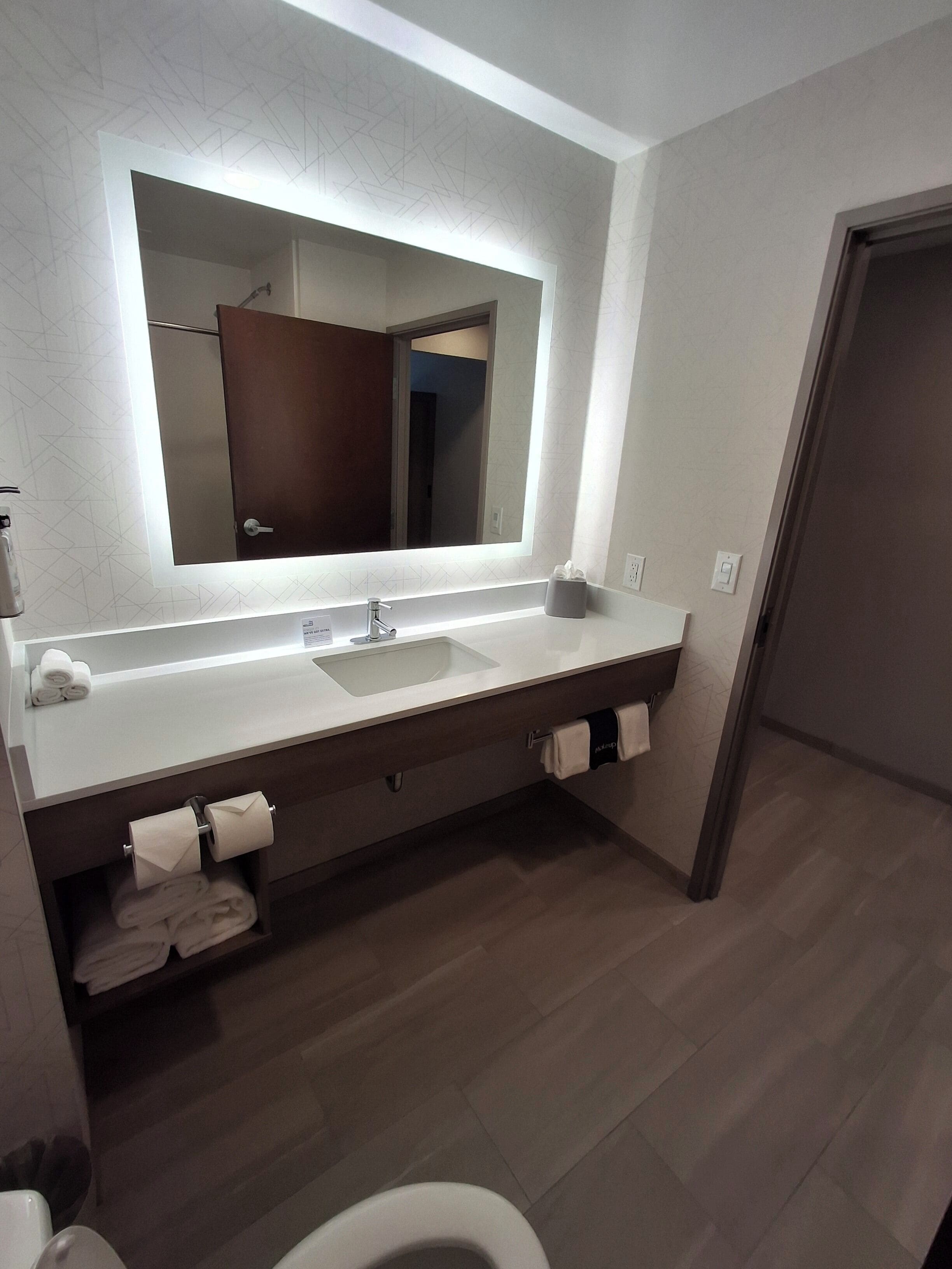A modern bathroom with a large mirror, a white sink, and a towel rack.