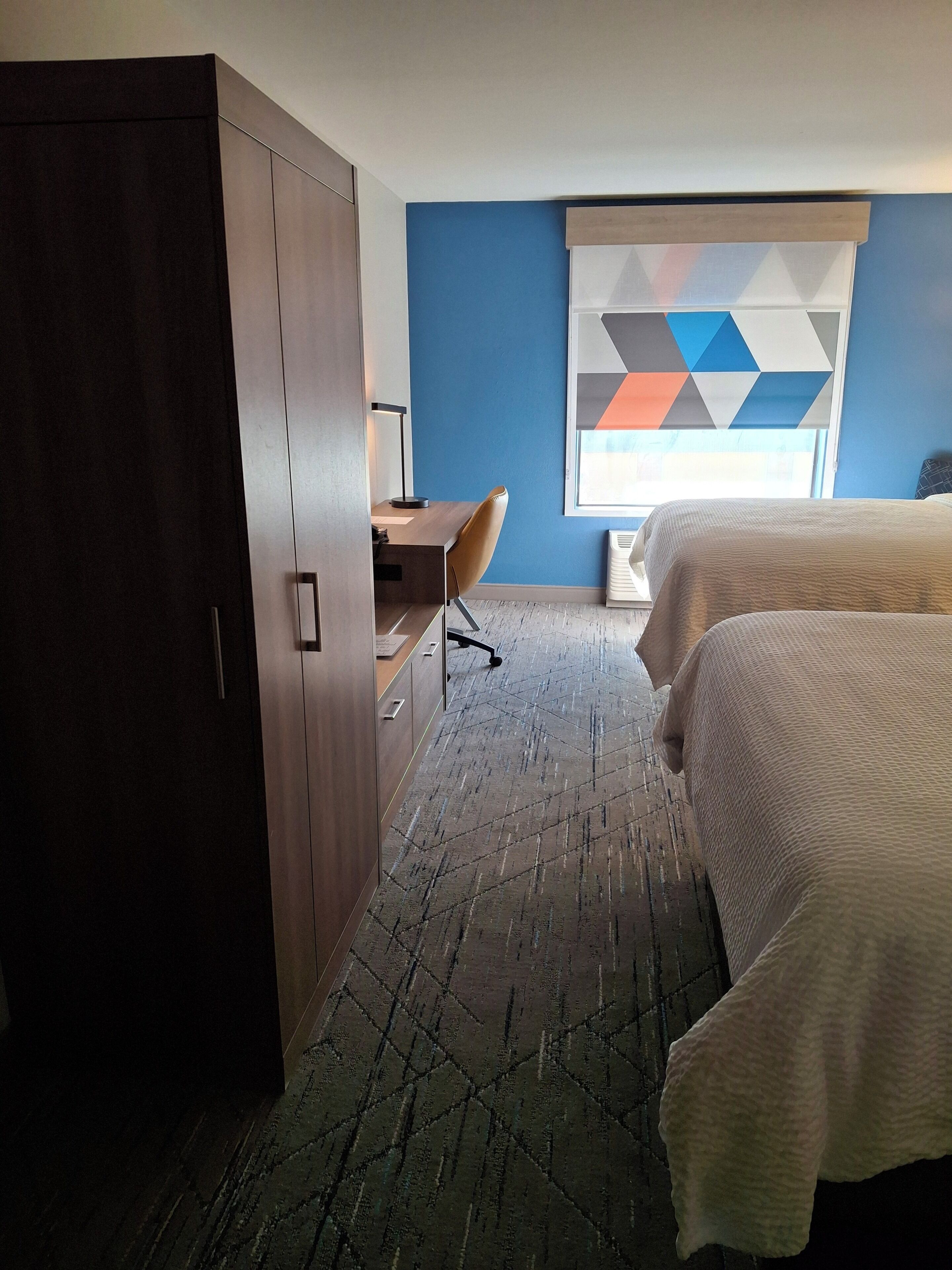 A hotel room with a desk, chair, and two beds.