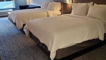 Quarto de hotel com duas camas, uma janela grande e design moderno.