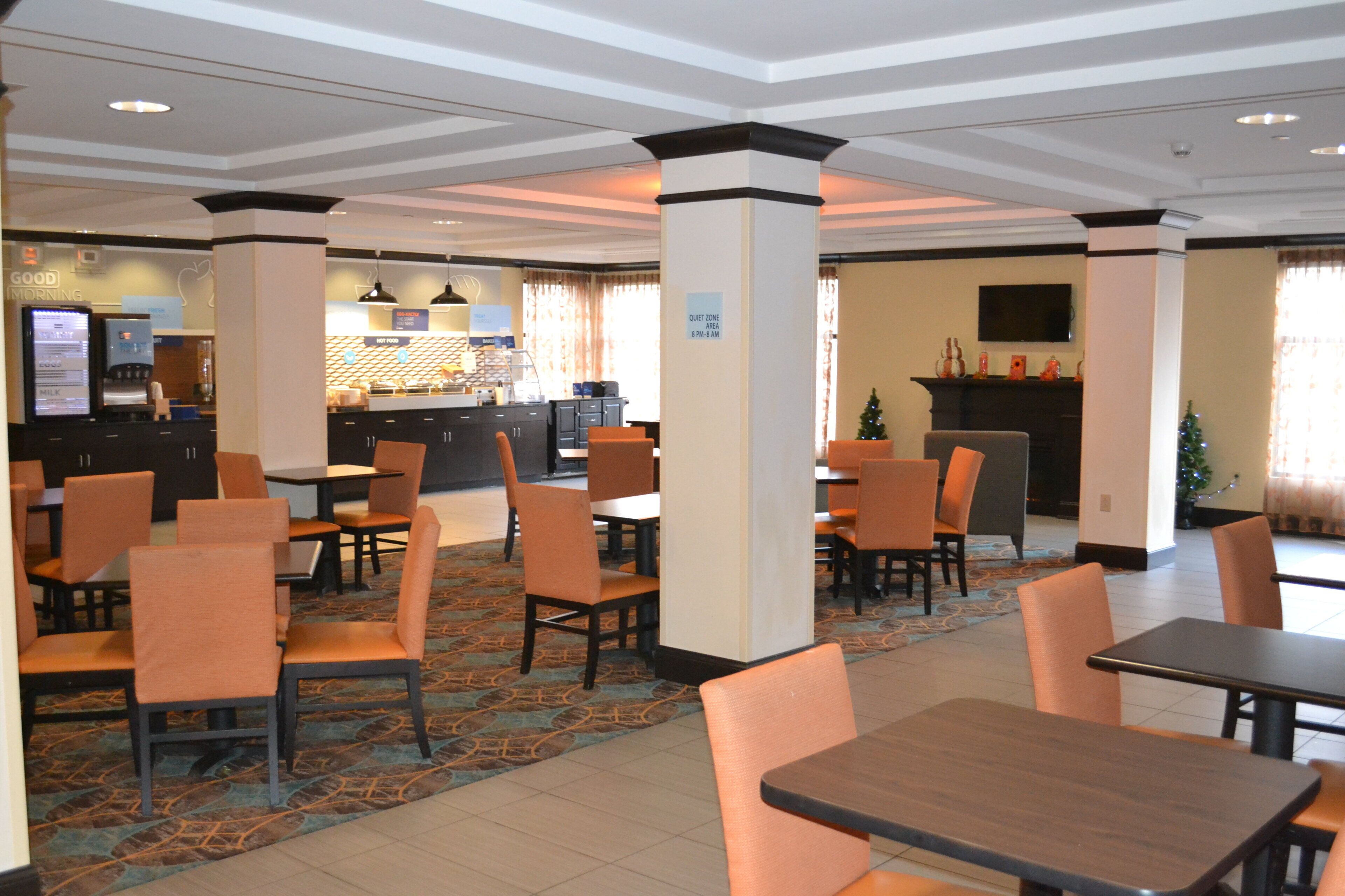 A hotel dining area with multiple tables and chairs, a coffee machine, and a sign indicating a quiet zone area.