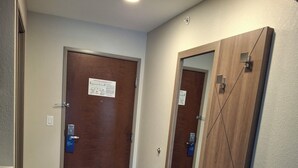 Un pasillo con una puerta de madera, un espejo con repisa y un accesorio de iluminación en el techo.