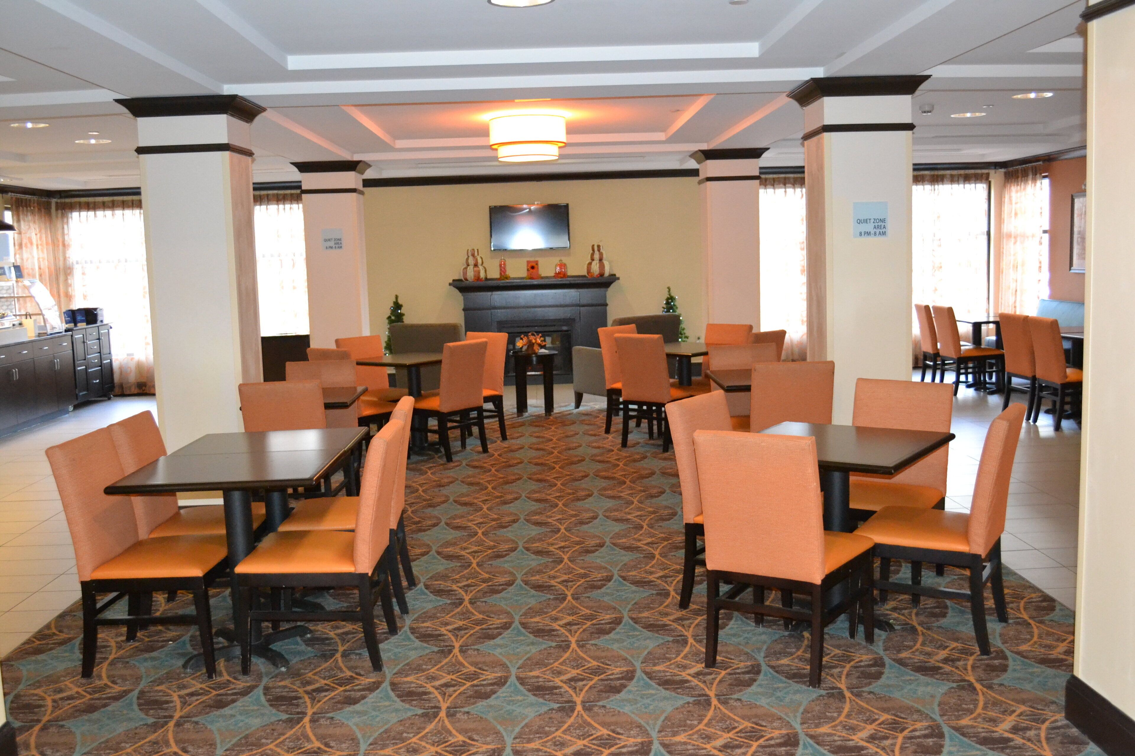 Comedor de hotel con mesas, sillas, chimenea y televisión en la pared.