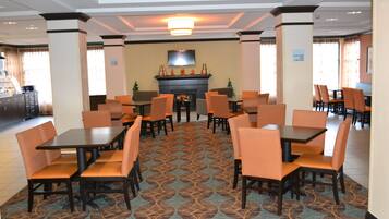 Comedor de hotel con mesas, sillas, chimenea y televisión en la pared.