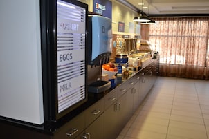 Zona de desayuno tipo buffet con estaciones de comida identificadas para huevos, leche y yogur.