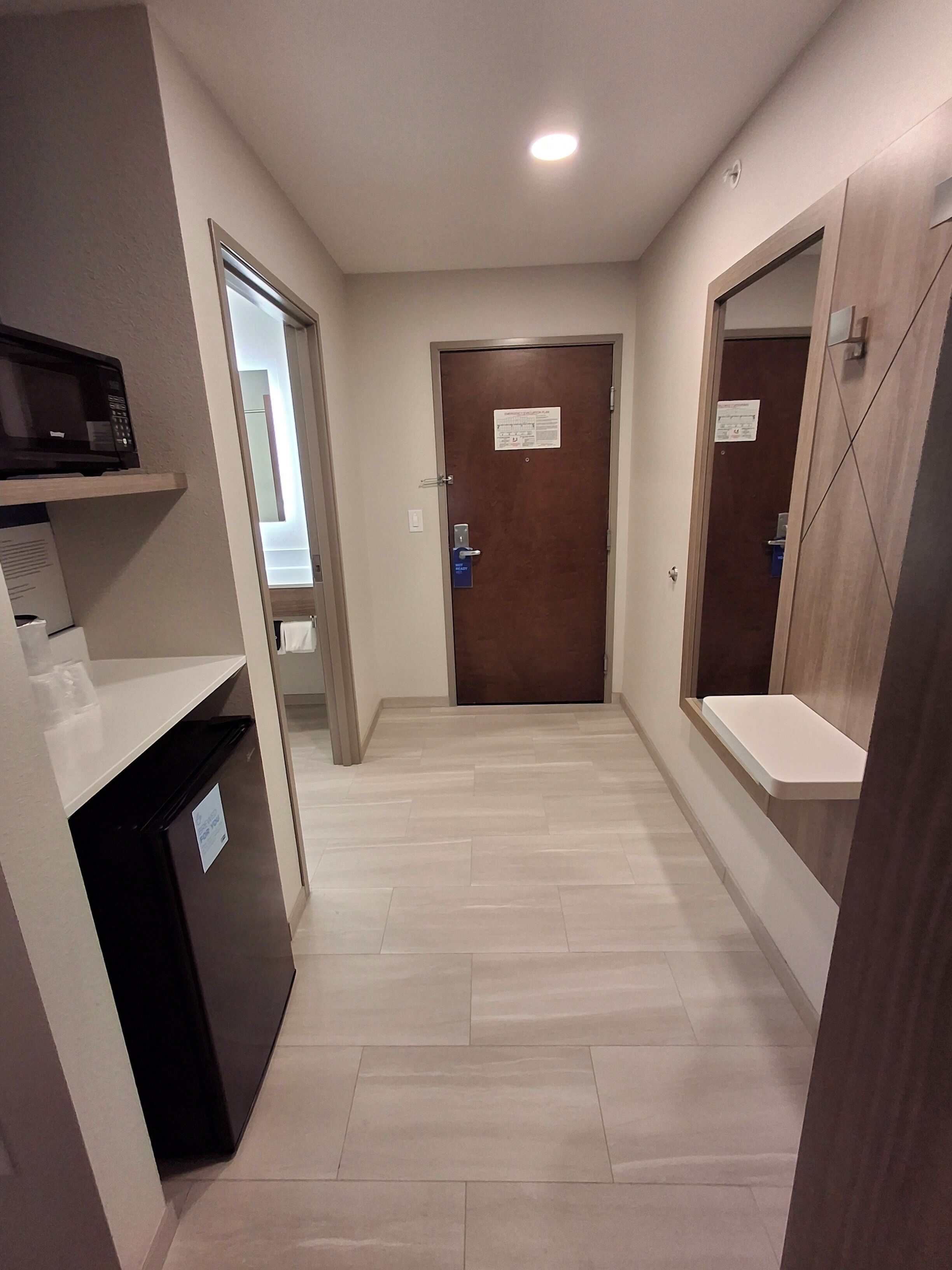 A hallway with a microwave on a shelf, a refrigerator, and a door with a sign.