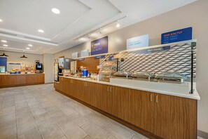 Espaço de café da manhã com estação de serviço, incluindo cereais, comida quente e uma seção de padaria.