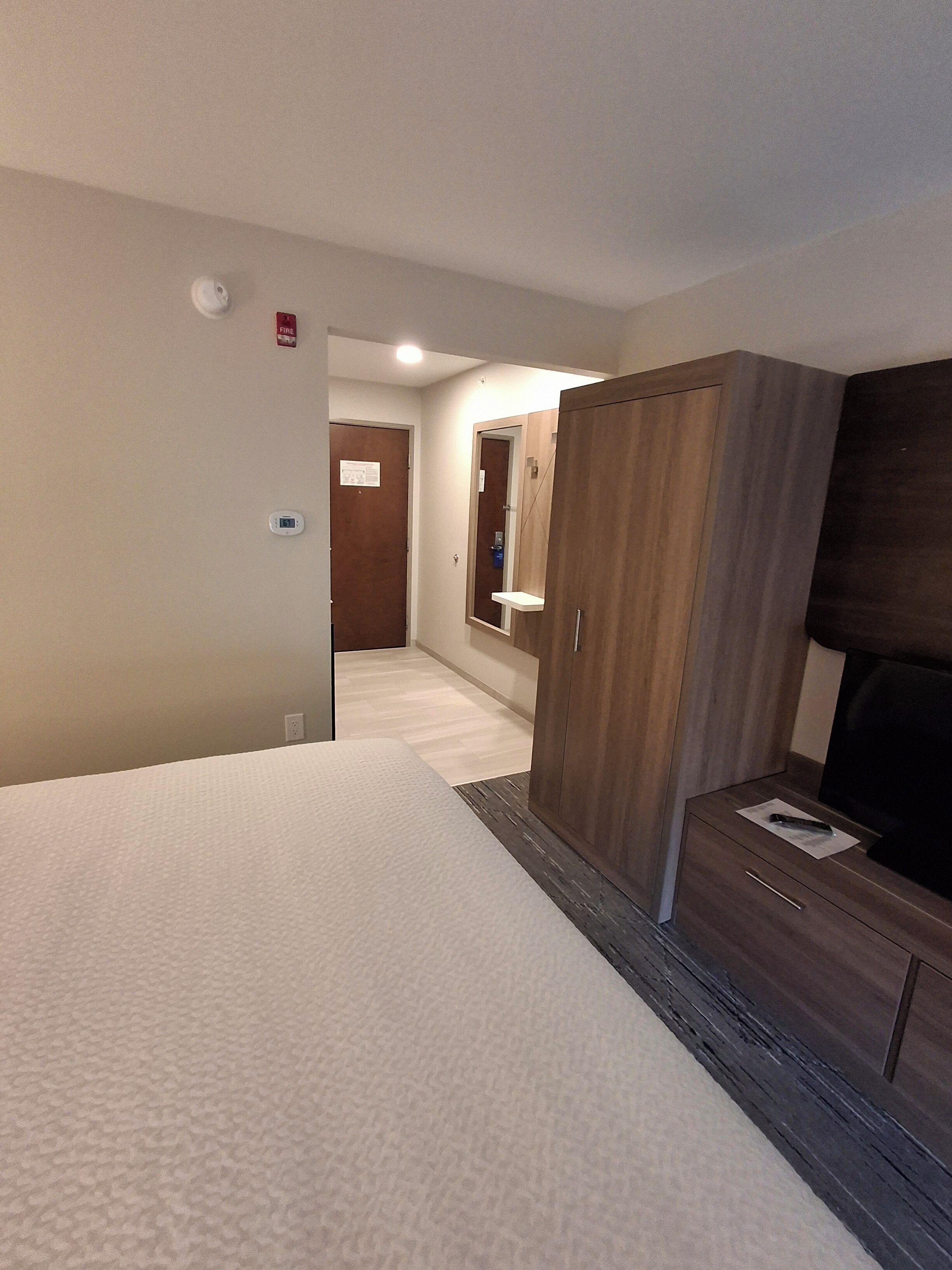 Una camera d'albergo con un letto, un armadio in legno, una piccola scrivania con televisore e uno specchio.