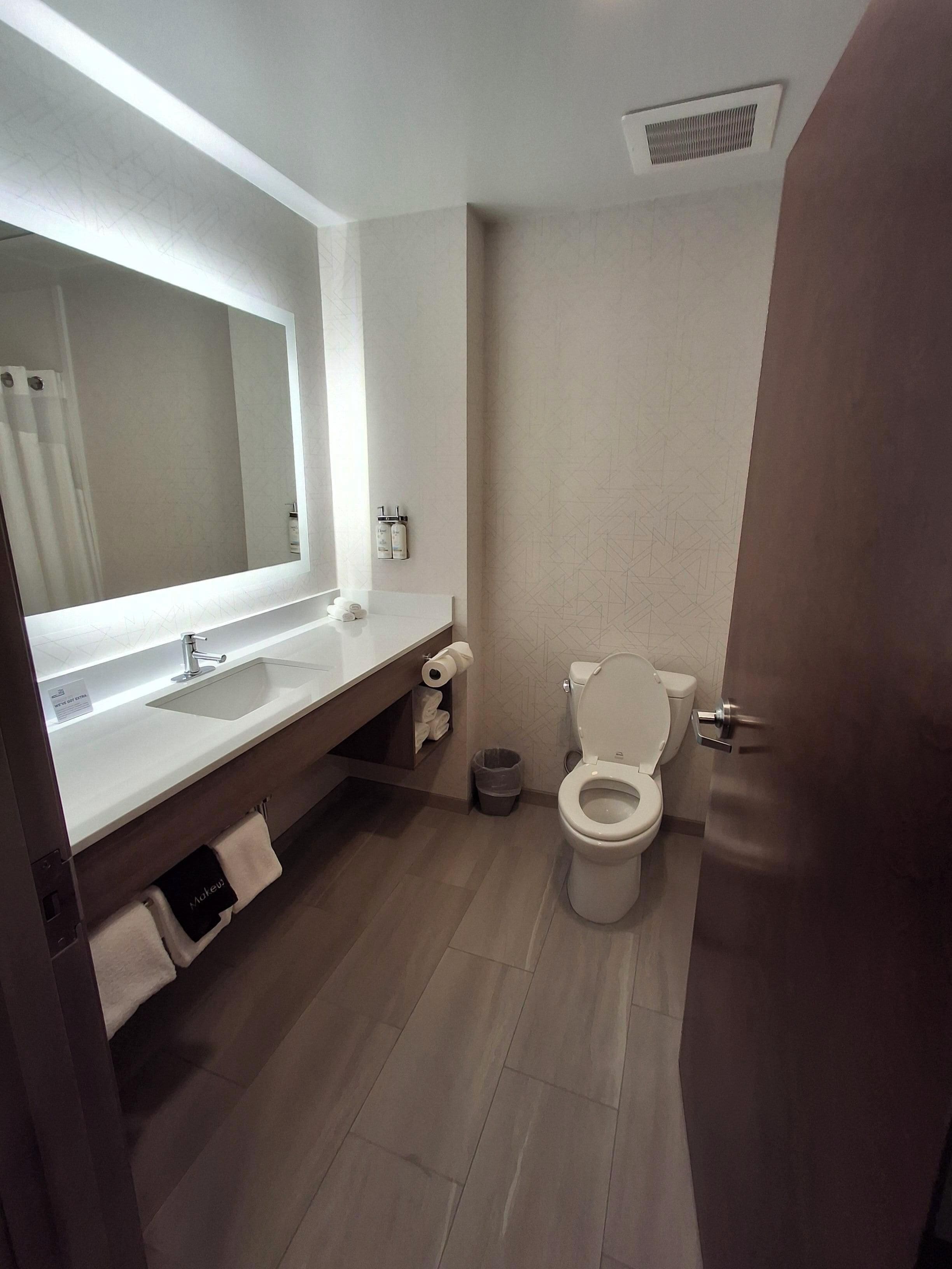A modern bathroom with a large mirror, a sink, and a toilet. There are towels and toiletries on the counter.