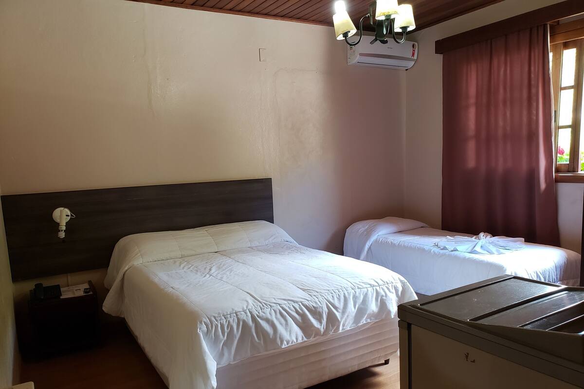 Habitación de hotel con dos camas, techo de madera, unidad de aire acondicionado y ventana con cortinas.