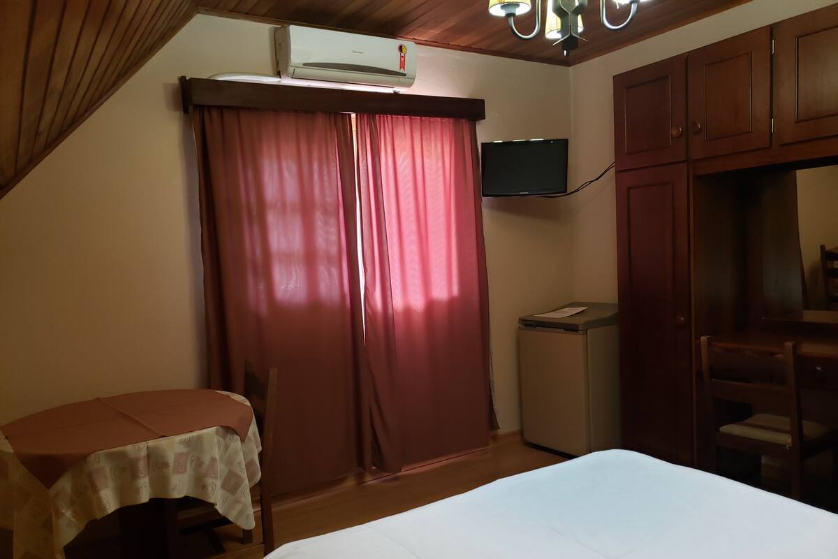 Un dormitorio con cama, escritorio, silla, televisor y aire acondicionado.