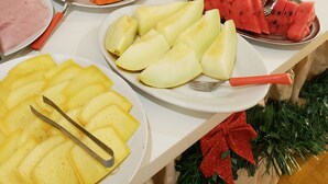 Una mesa de buffet con diversos alimentos, como pasteles, frutas y una bandeja de jamón.