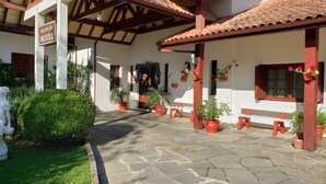 Una entrada de hotel con un patio empedrado, plantas en macetas y bancos de madera.