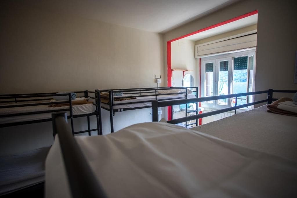 A dormitory room with bunk beds, a window with blinds, and a door leading to an outdoor area.