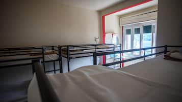 A dormitory room with bunk beds, a window with blinds, and a door leading to an outdoor area.