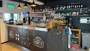 Een bar met een toonbank, flessen, glazen en een koffieapparaat.