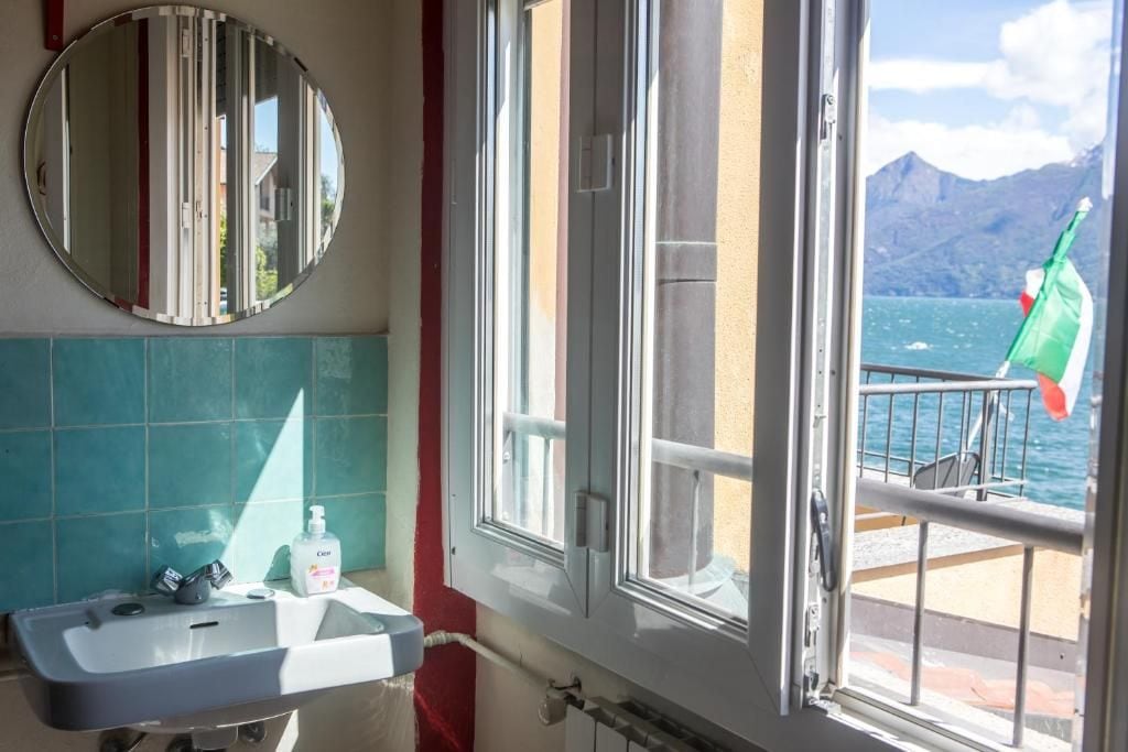 Ein Badezimmer mit Waschbecken, Spiegel und Fenster mit Blick auf ein Gewässer und Berge.