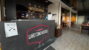 Een hostel interieur met een 'Welcome' bord, een bord voor huurkayaks en een 'Lake Como Hostels' bord.